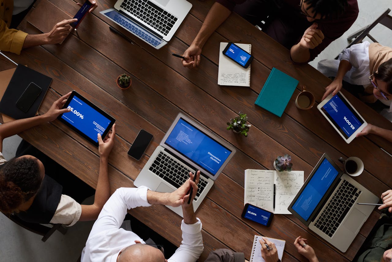 Services Overhead view of a diverse team discussing around a wooden table, using technology.